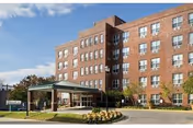 Brick senior living building with a covered entrance and landscaped front yard.