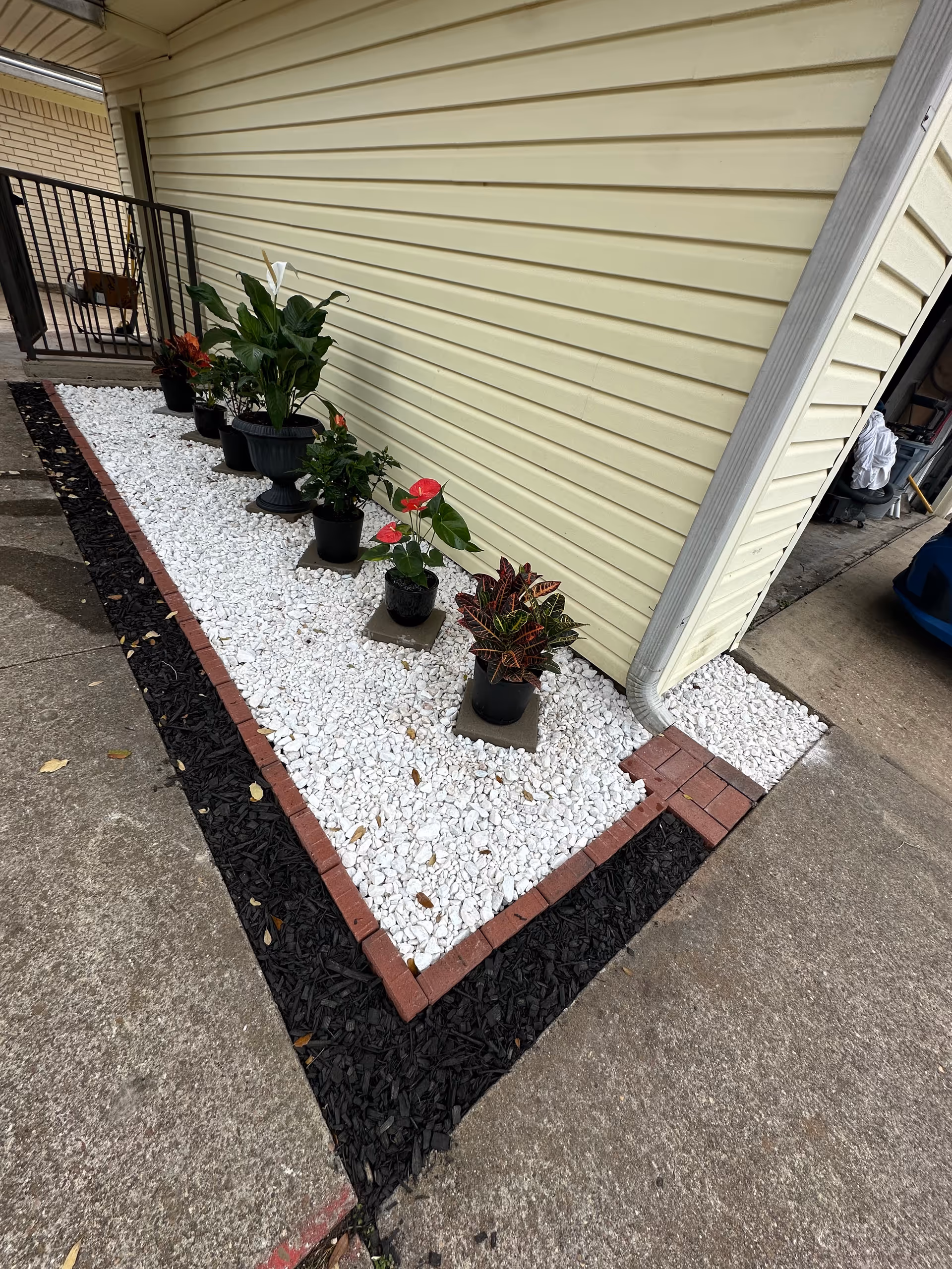 Exterior view of a beige wall with white rock garden and potted plants
