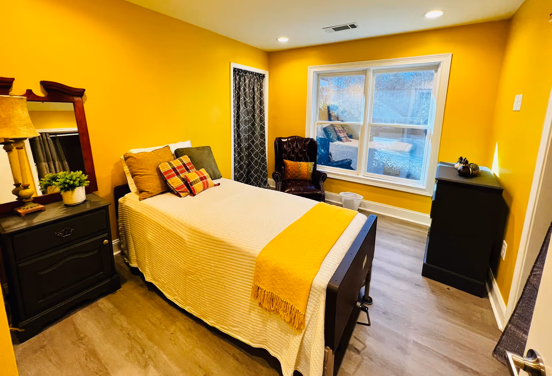 Bright yellow bedroom featuring a bed, dresser, chair, and large window.