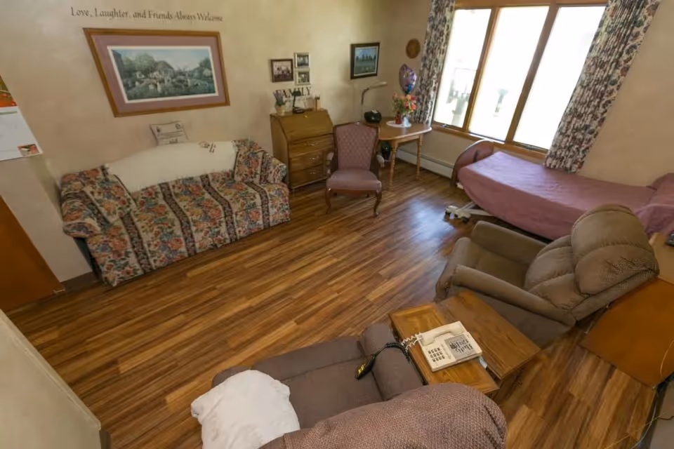 Cozy living room in a senior facility with floral sofa, recliner, and large window.
