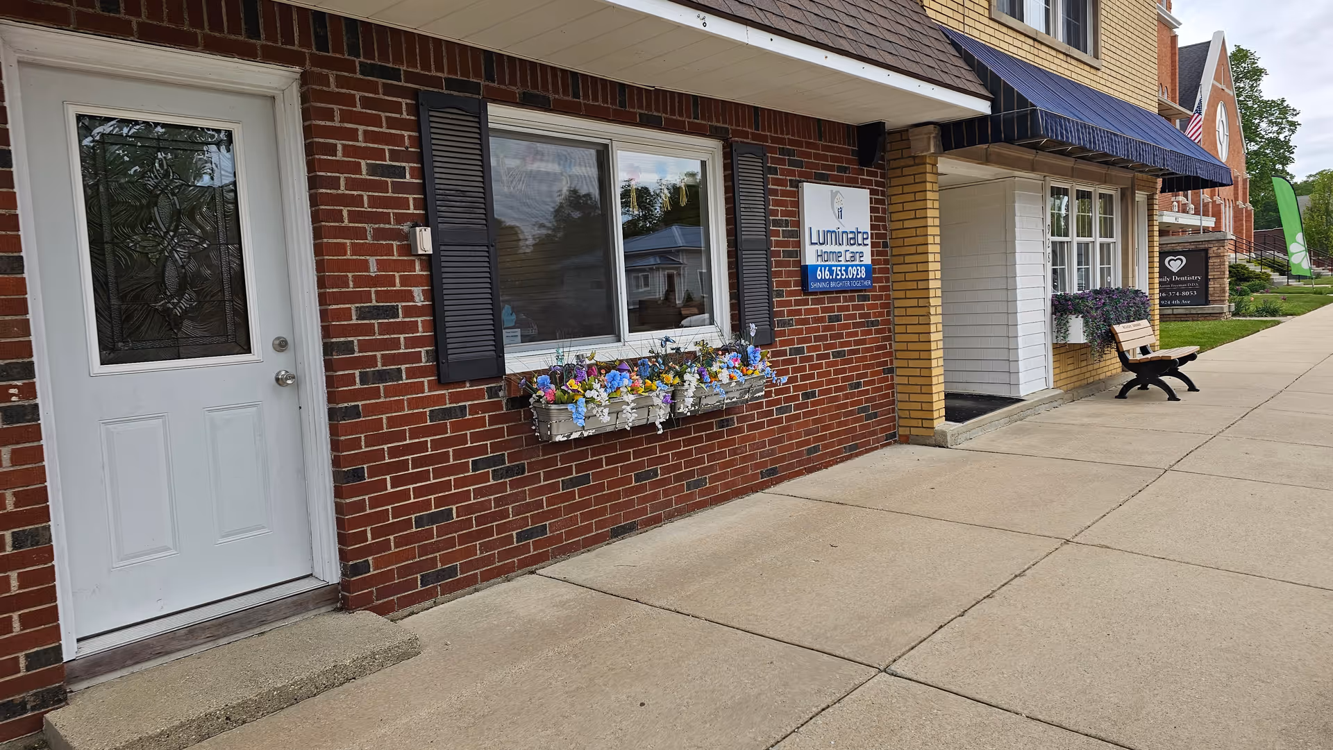Exterior view of Luminate Home Care storefront with flower boxes and a bench.