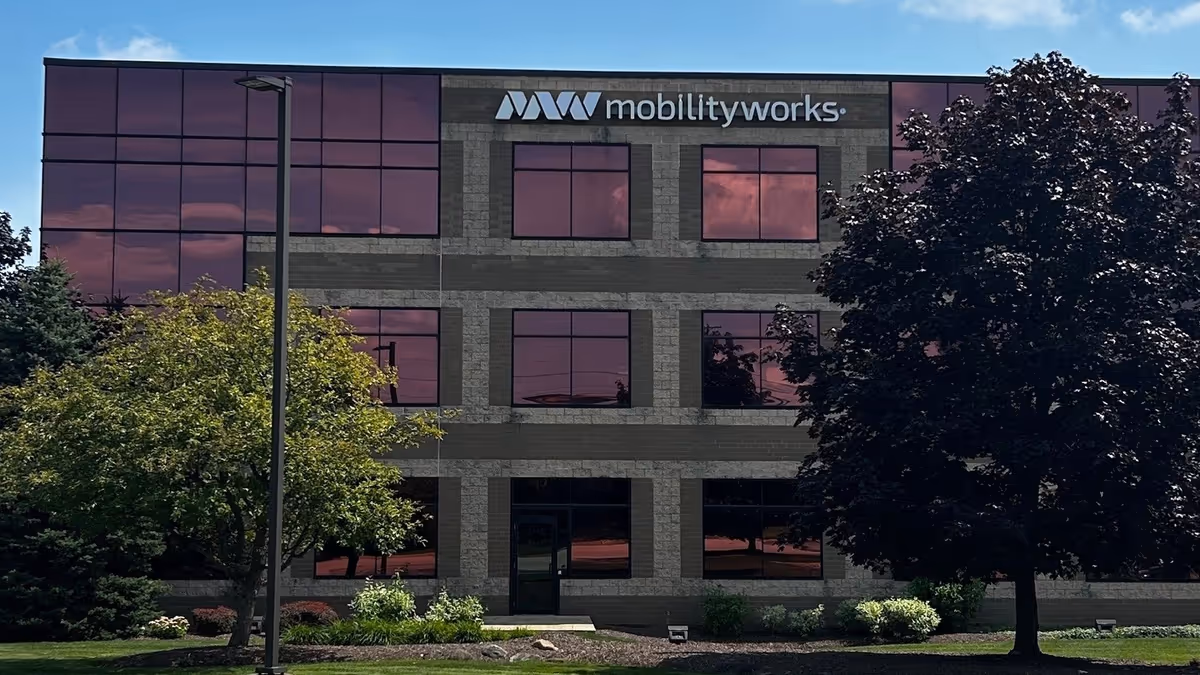 Three-story MobilityWorks corporate office building with brick facade, maroon-tinted windows, and trees nearby.