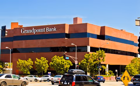 Exterior view of a brick Grandpoint Bank building with cars and trees.