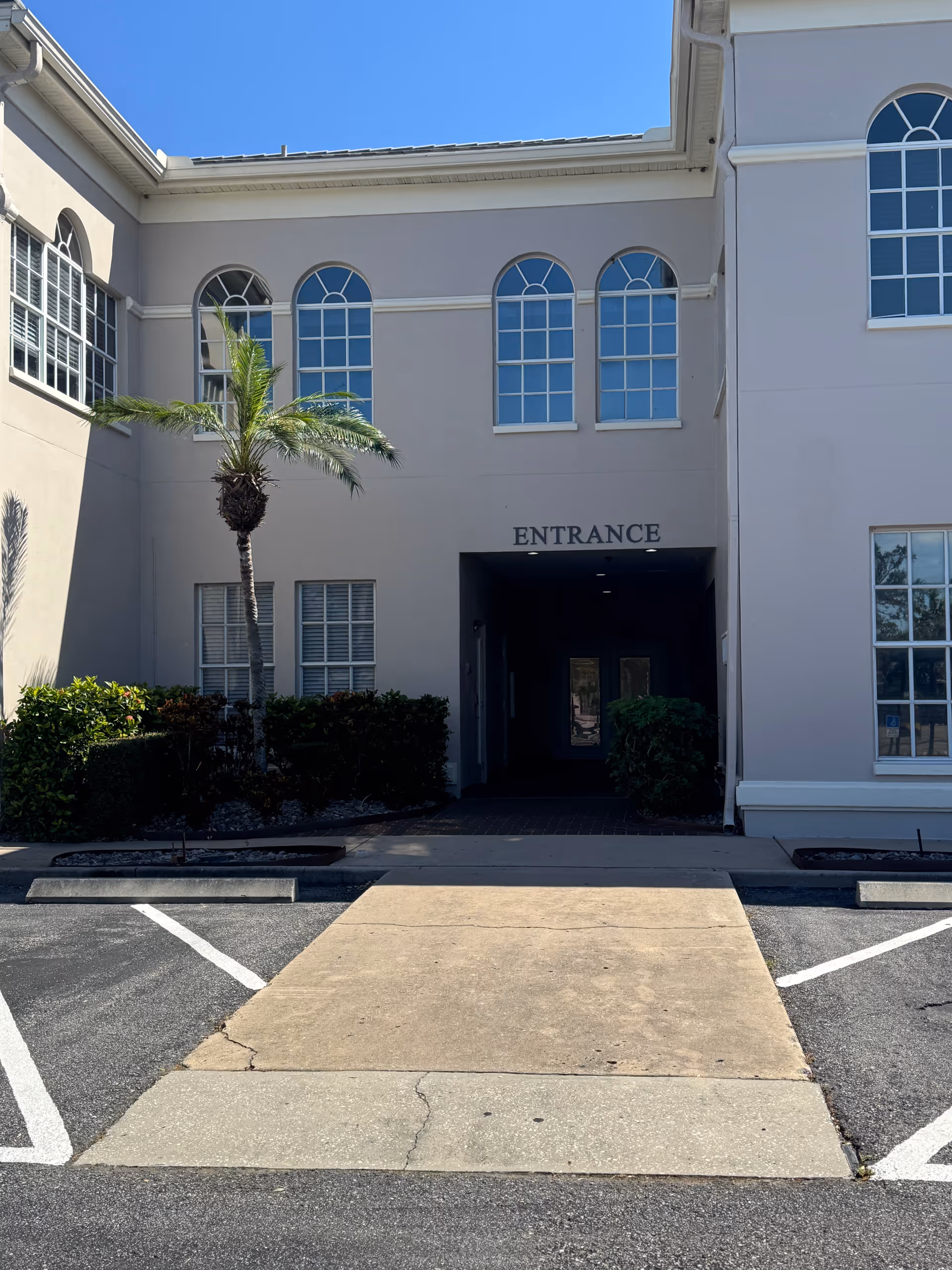 Front exterior of a beige senior living building with arched windows and an entrance.