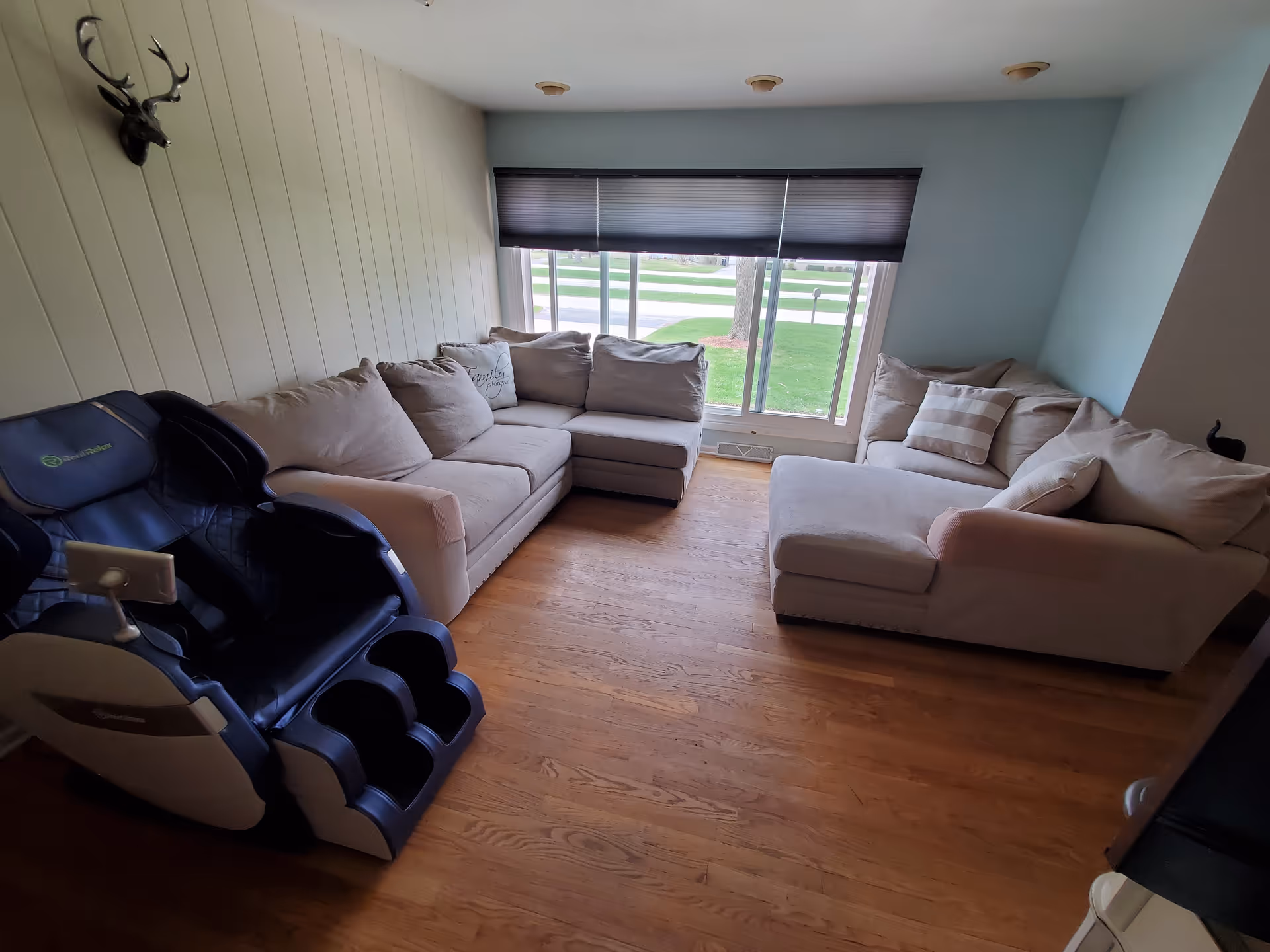 Cozy living room with beige sectional sofa, massage chair, and large window overlooking green lawn.