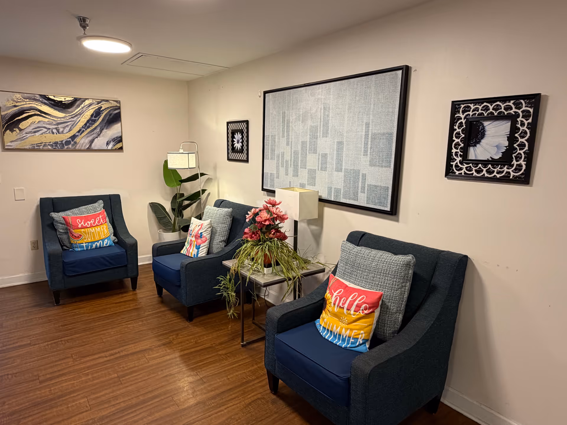 Cozy waiting area with three blue armchairs, colorful pillows, a plant, and wall art.
