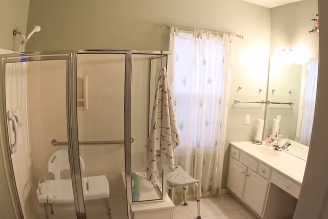 Accessible bathroom with glass shower, shower chair, and long vanity.
