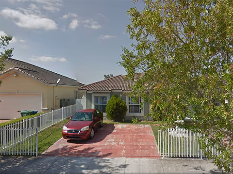 Single-story senior care center exterior with a red driveway, white fence, and a parked car.