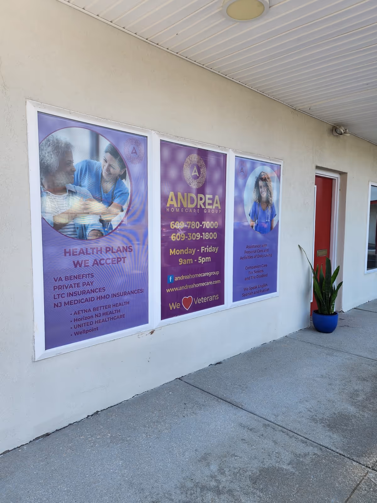 Exterior wall with three Andrea Homecare Group posters and a red door beside a blue planter.