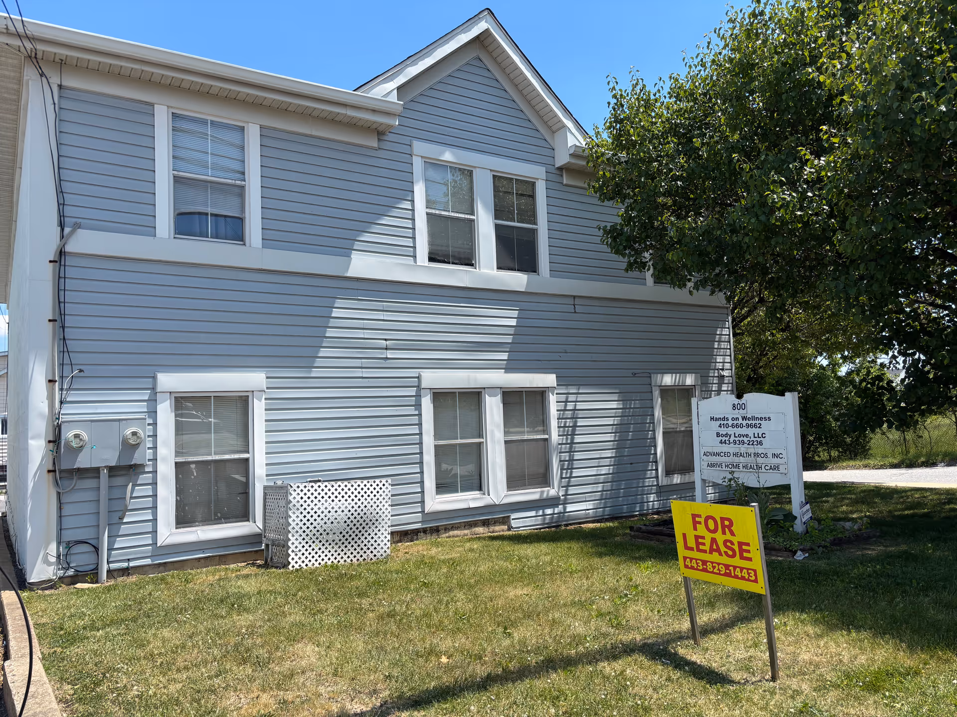A two-story blue building with white trim and a FOR LEASE sign in the yard.