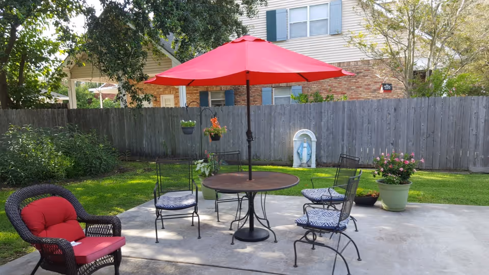 Outdoor patio with round table, red umbrella, metal chairs, and potted plants.