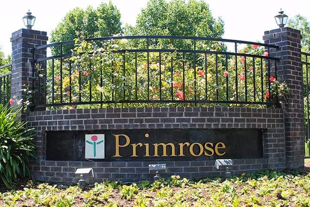 Brick sign with Primrose logo and railing at the facility entrance surrounded by greenery