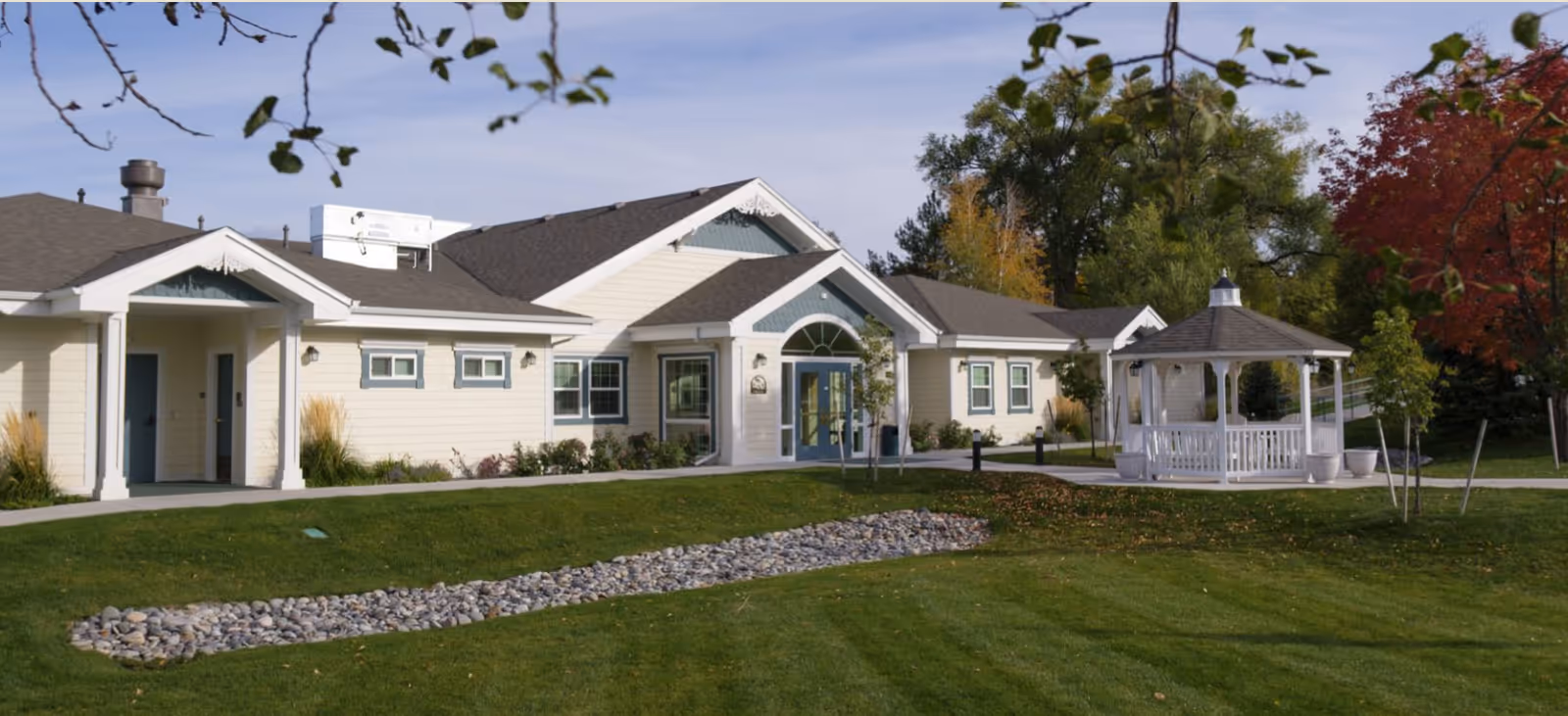 Single-story senior living facility with white exterior, front entrance, and white gazebo on green lawn