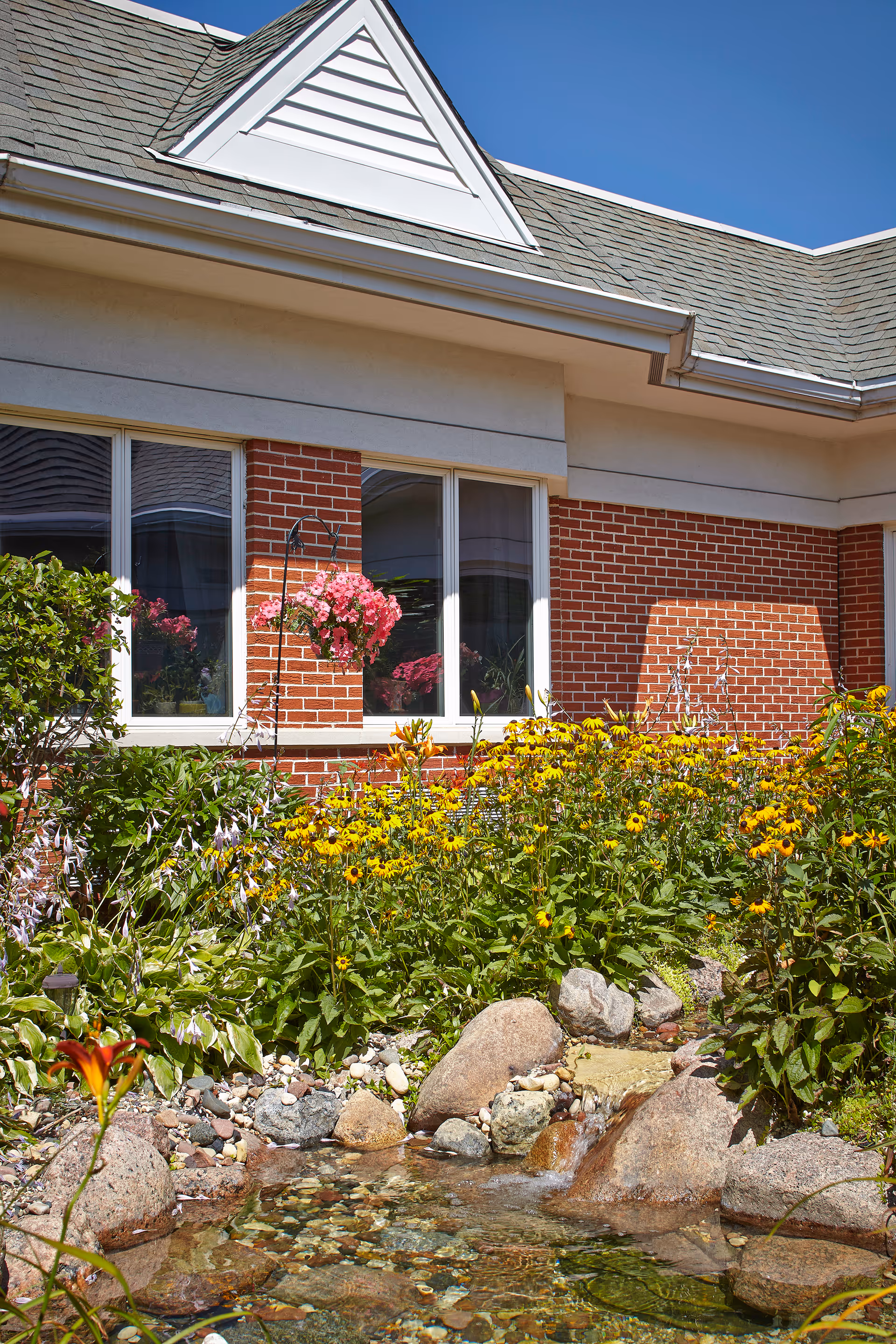 Brick exterior of Alta Rehab at Oak Brook with colorful garden and rock waterfall.