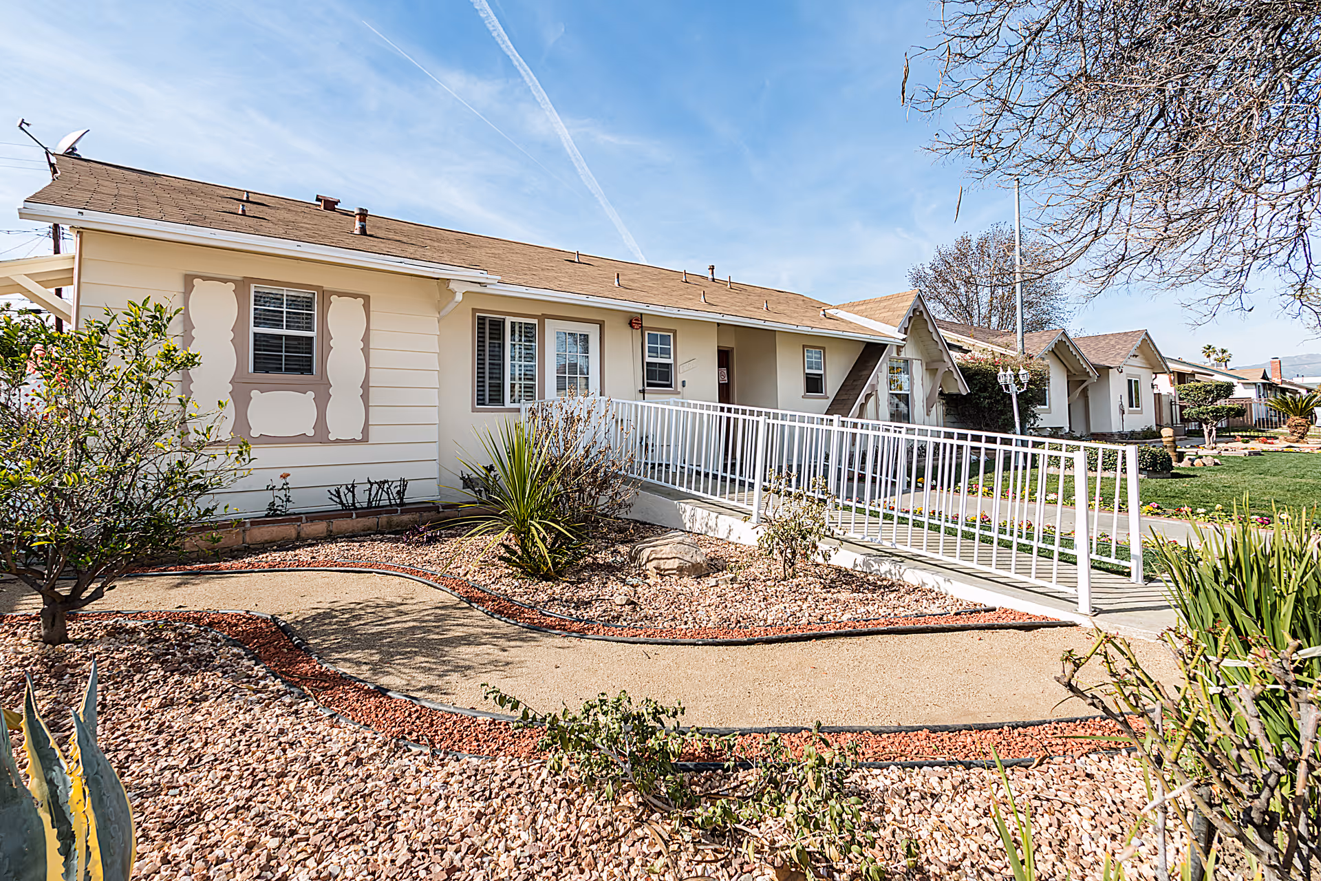 Single-story beige senior care home with ramp and desert landscaping in front