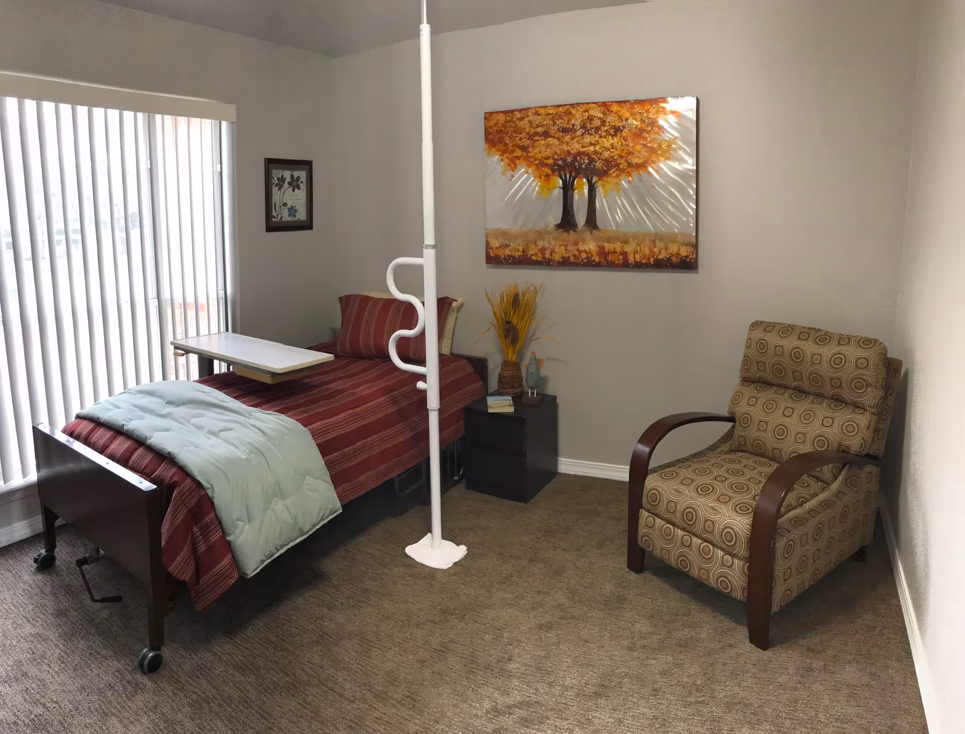 A small bedroom in a senior living facility with a bed, chair, and artwork.
