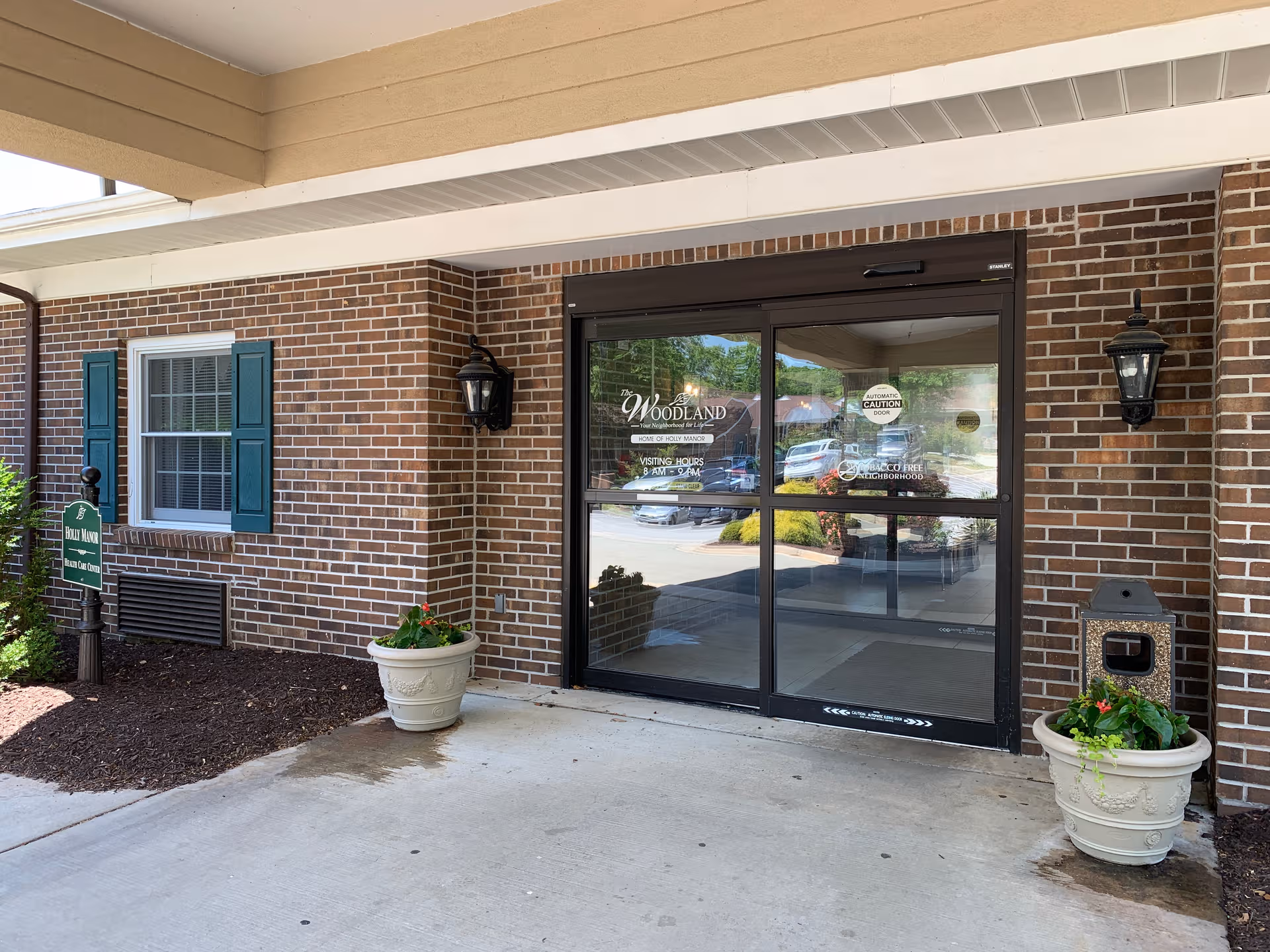 The Woodland entrance of a brick senior living facility with glass doors and planters.