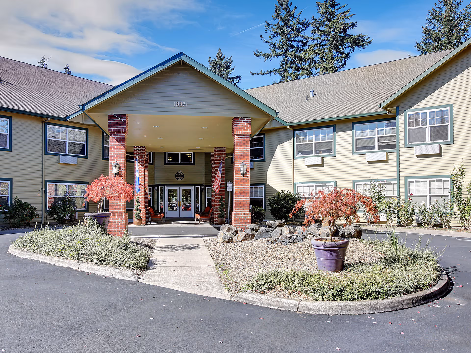 Exterior view of Prestige Senior Living Riverwood entrance with brick pillars and landscaping.