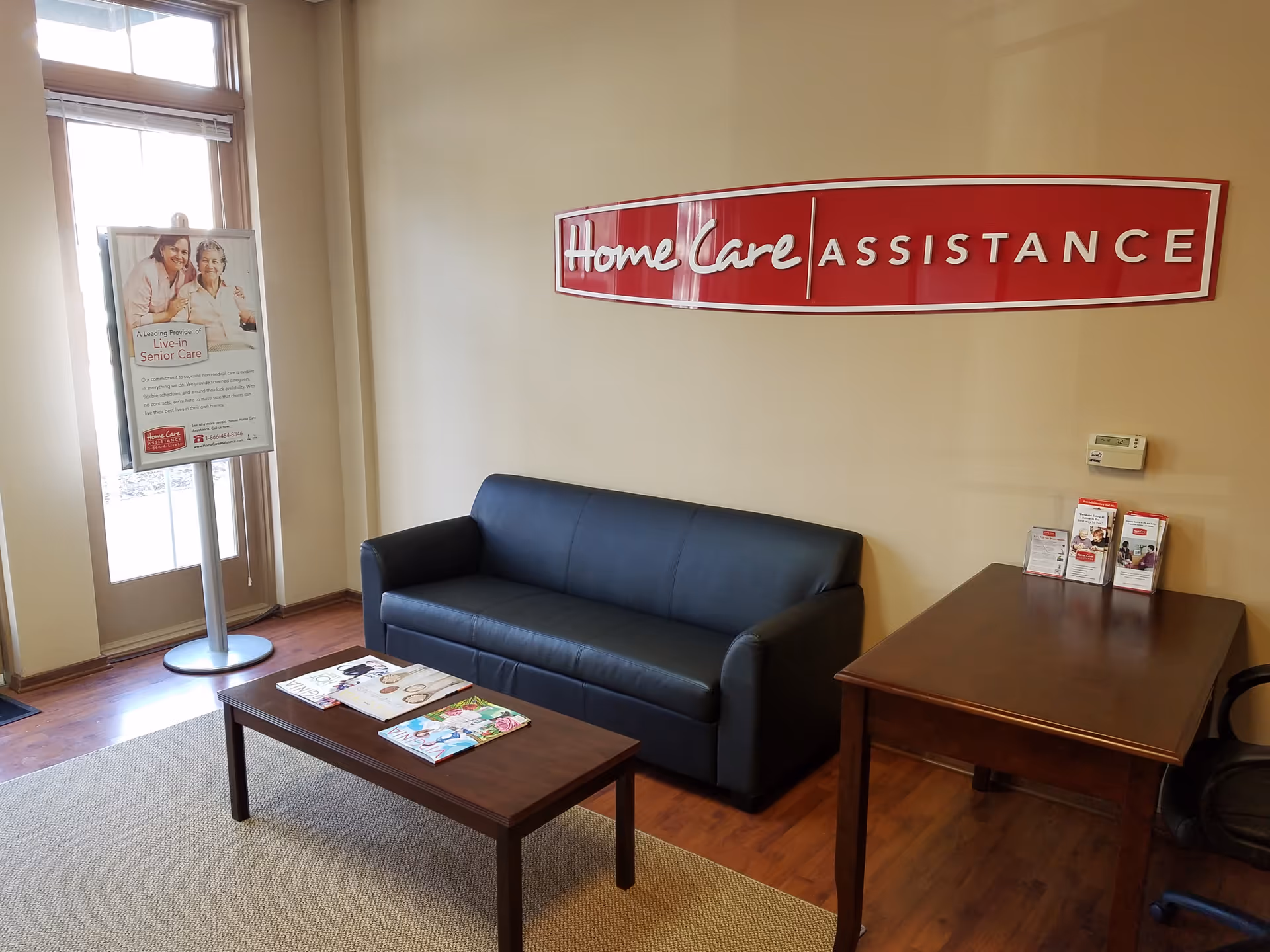 Interior lobby of a senior care facility with a sofa, desk, and red sign.