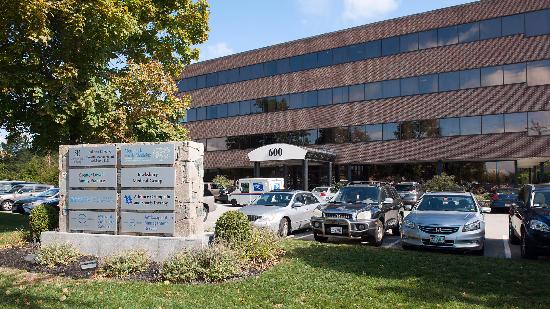 Front exterior of a brick medical building with a parking lot and stone sign.