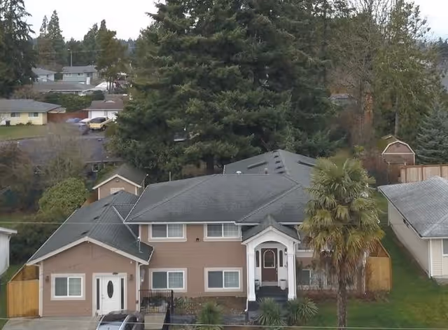 Front view of a suburban house with driveway, trees, and a palm tree.