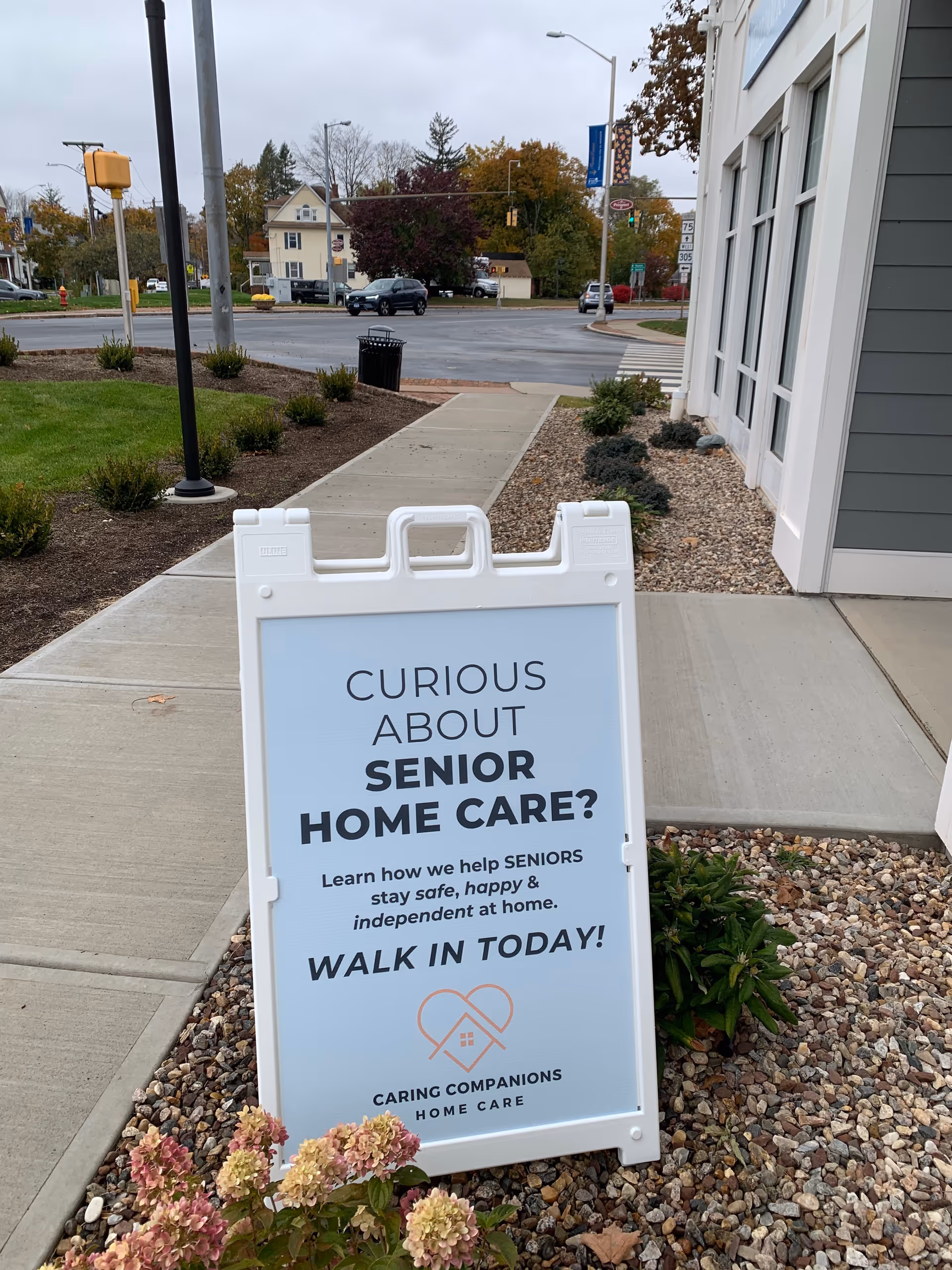 Outdoor sidewalk in front of Caring Companions Home Care building with a large promotional sign.
