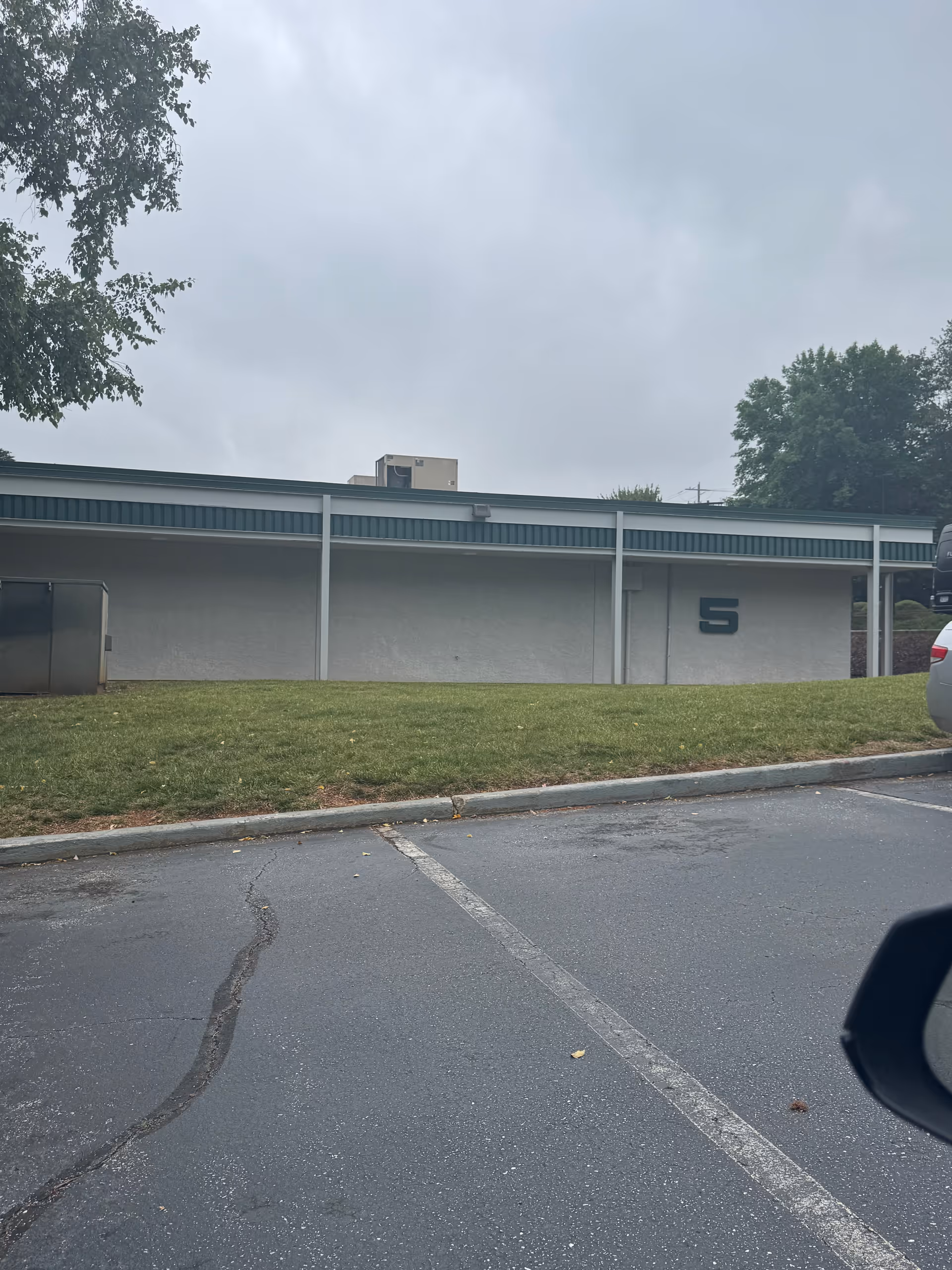 Exterior view of a low gray facility wall with a large number 5, parking lot.