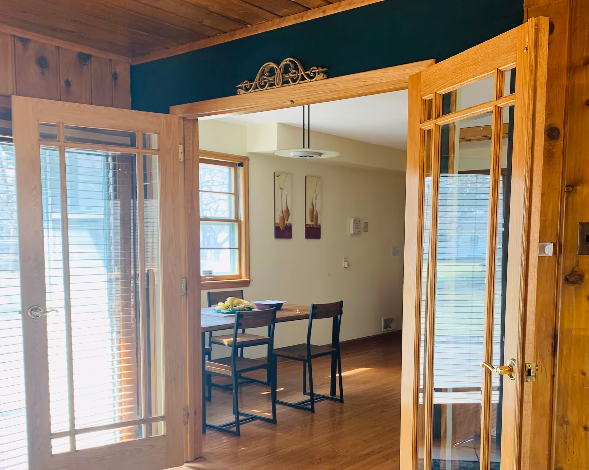 Open wooden French doors reveal a dining area with a table and chairs.