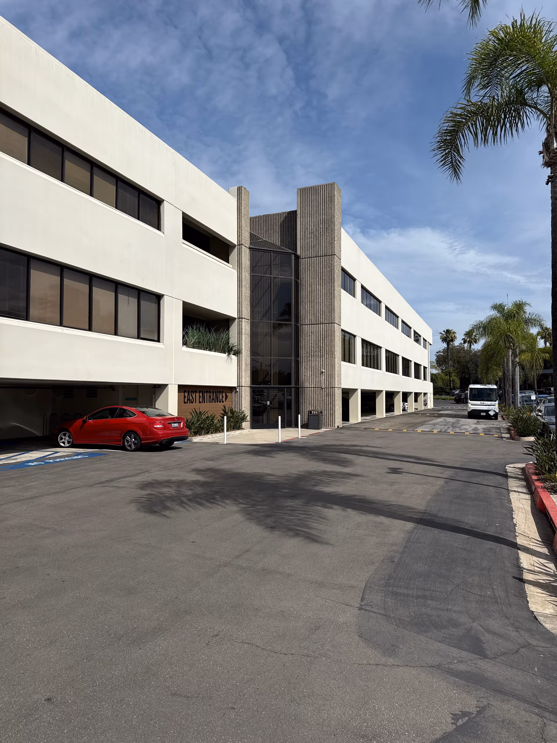 Exterior view of a modern senior care facility with palm trees and a parking lot.