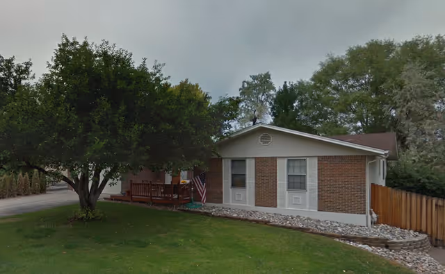 Exterior view of a brick assisted living building with a small front deck and lawn.