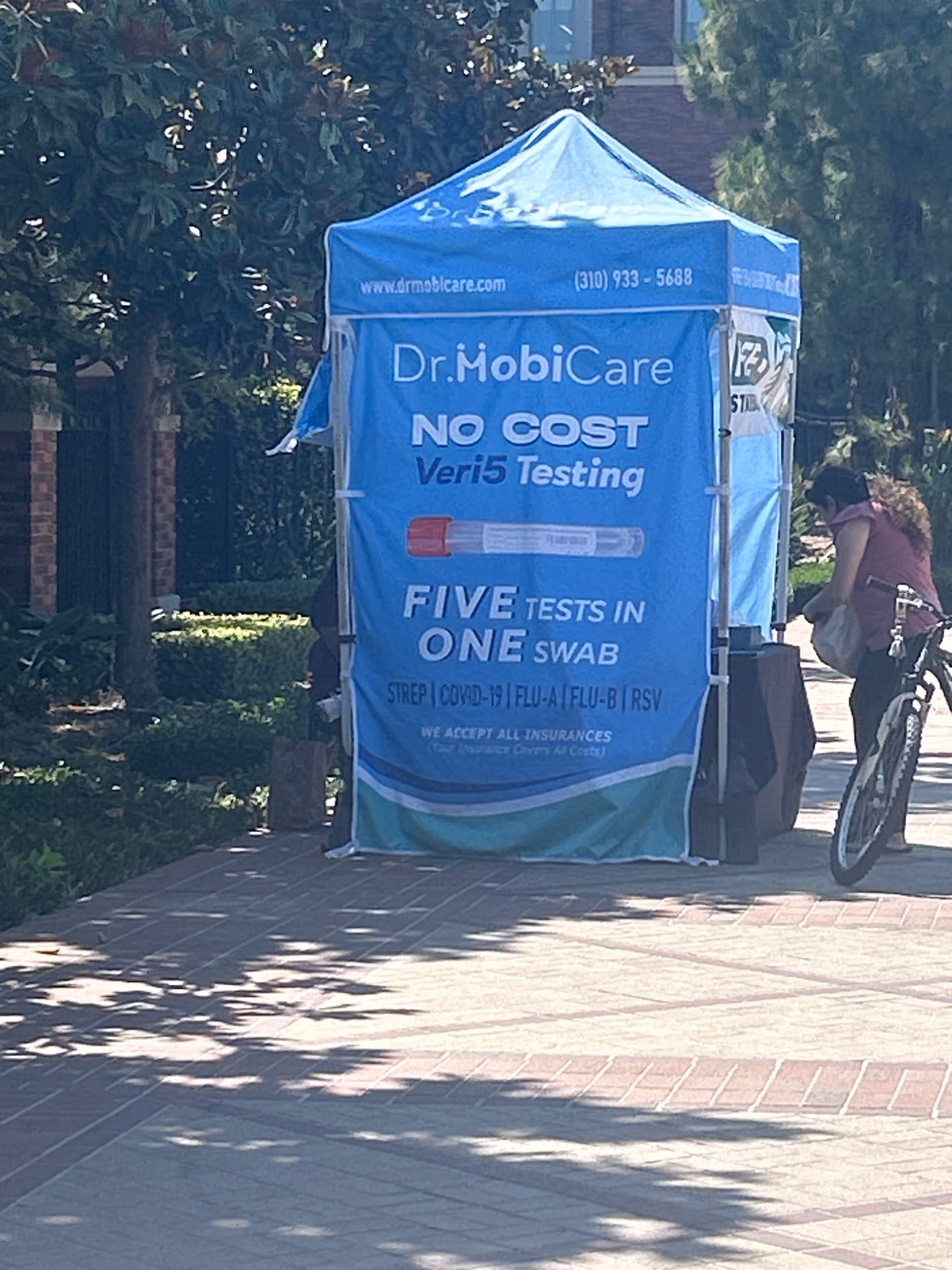 Blue Dr. MobiCare tent with testing signage on a sunny outdoor sidewalk.