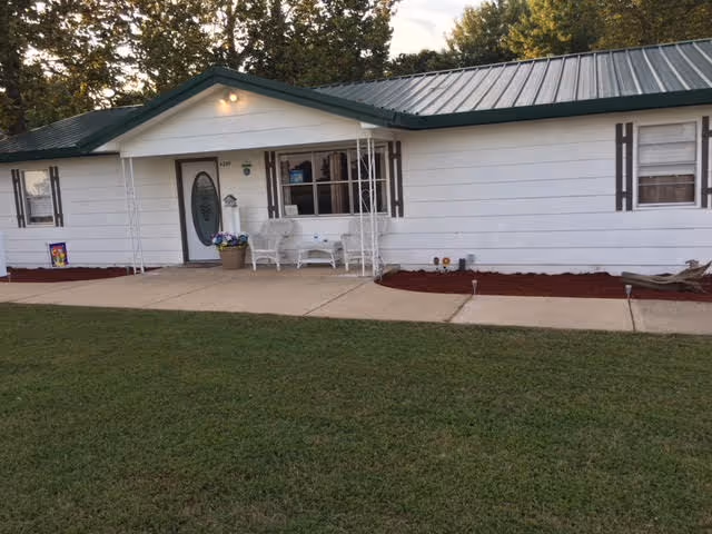 White single-story facility with green roof, front porch seating, and a trimmed flower bed.
