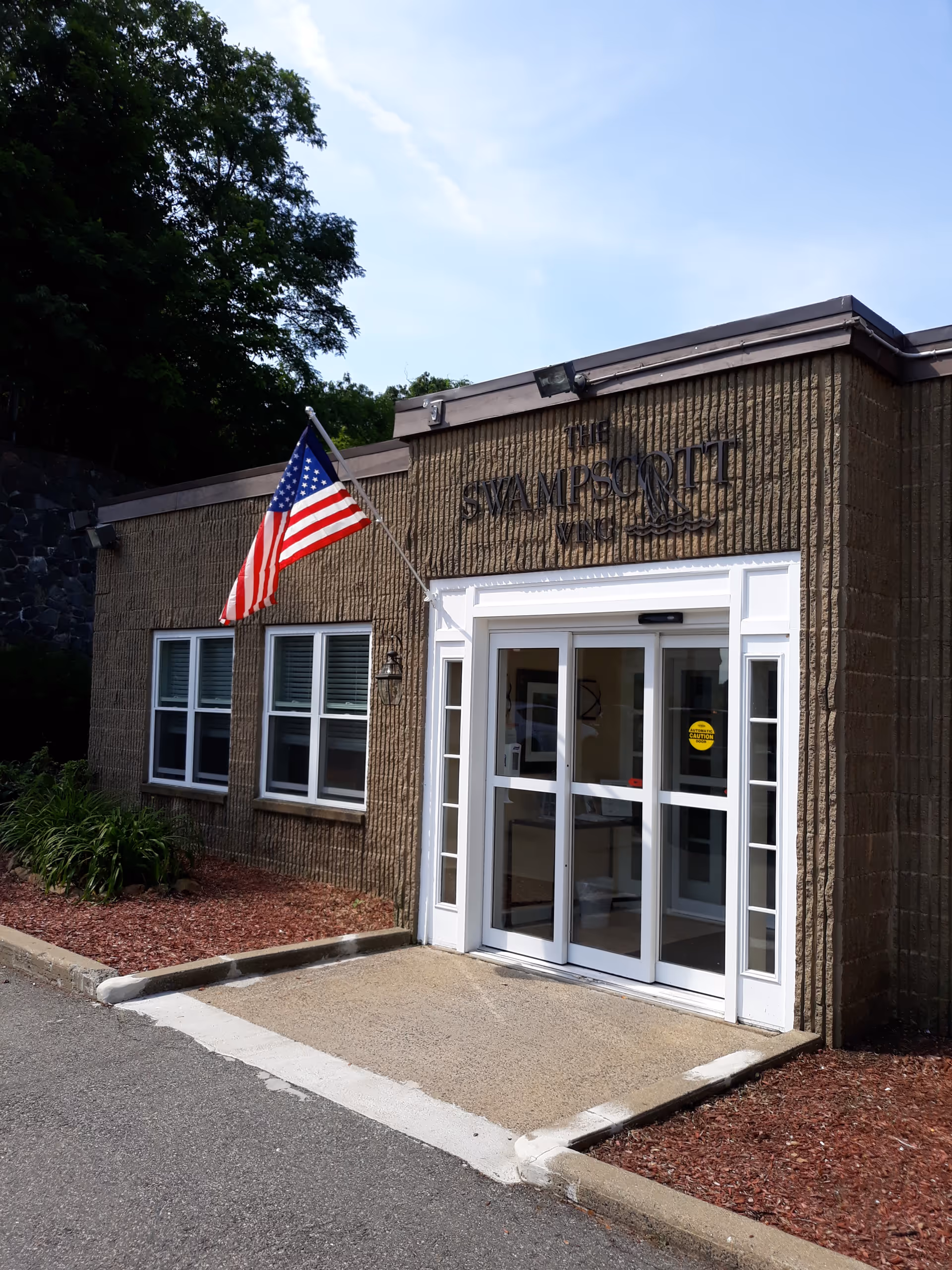 Front exterior of a brick facility with glass doors and an American flag