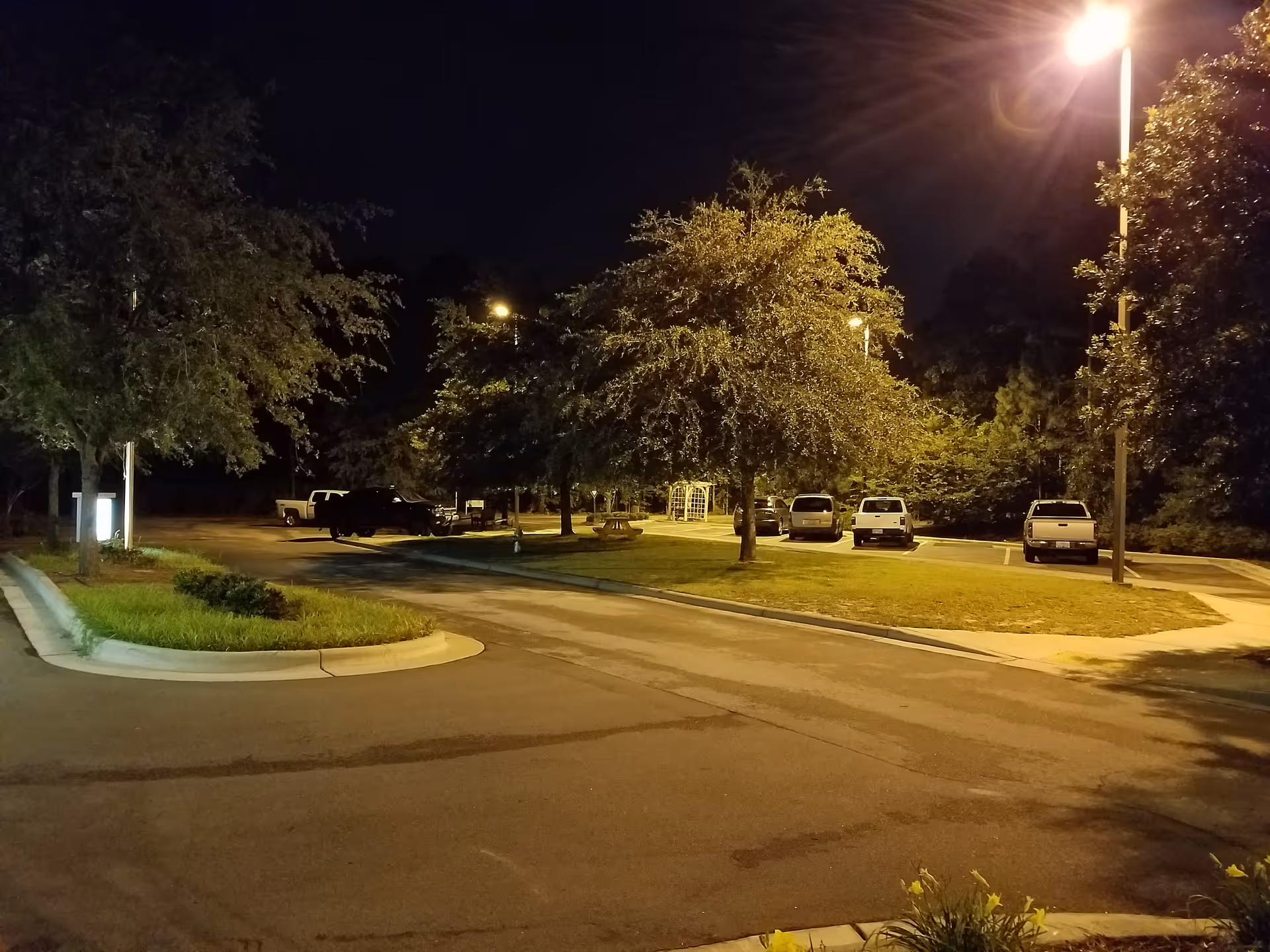 Nighttime exterior of a parking lot at the facility with trees and parked cars.