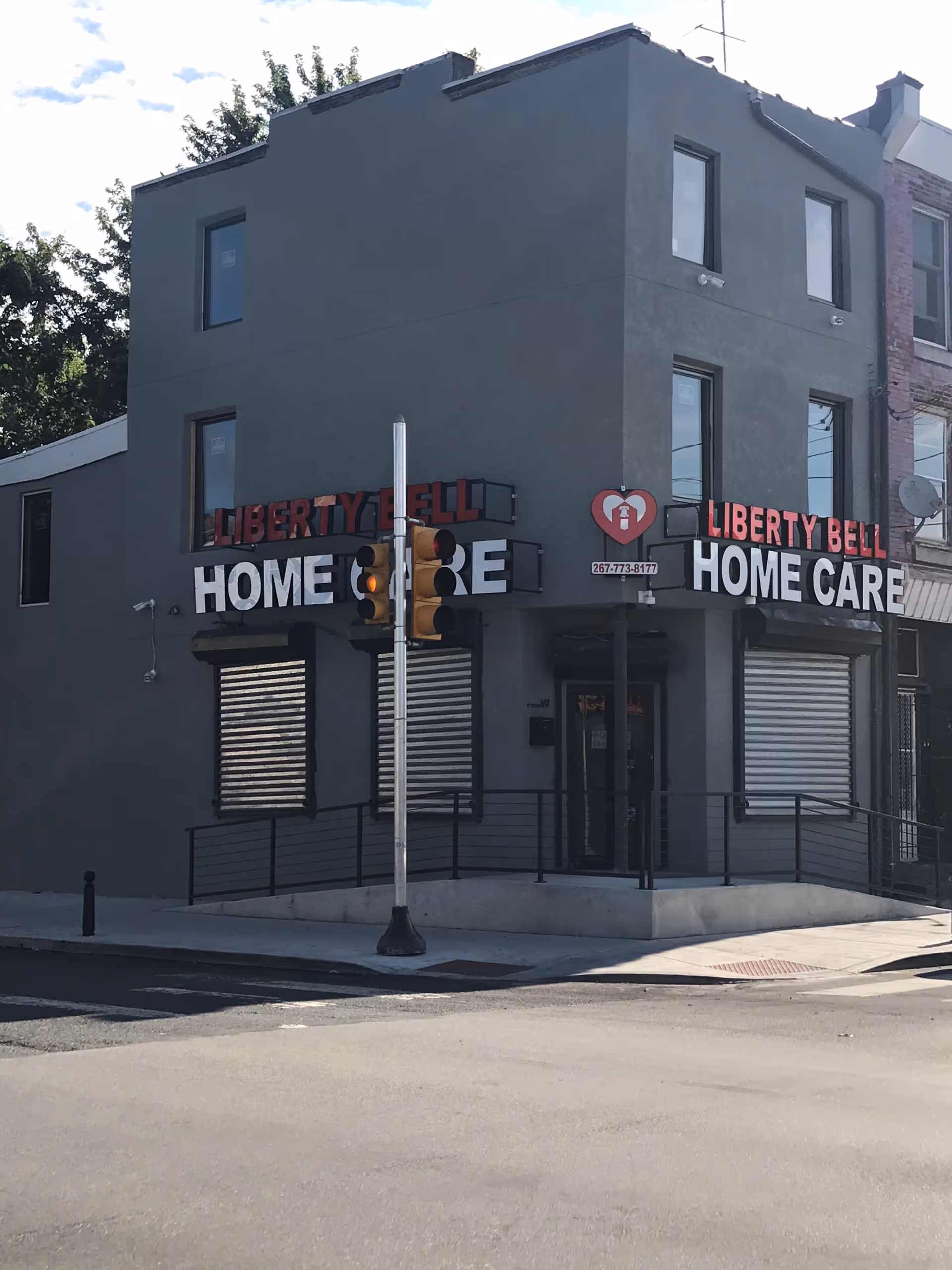 Grey three-story building on a street corner with Liberty Bell Home Care signage