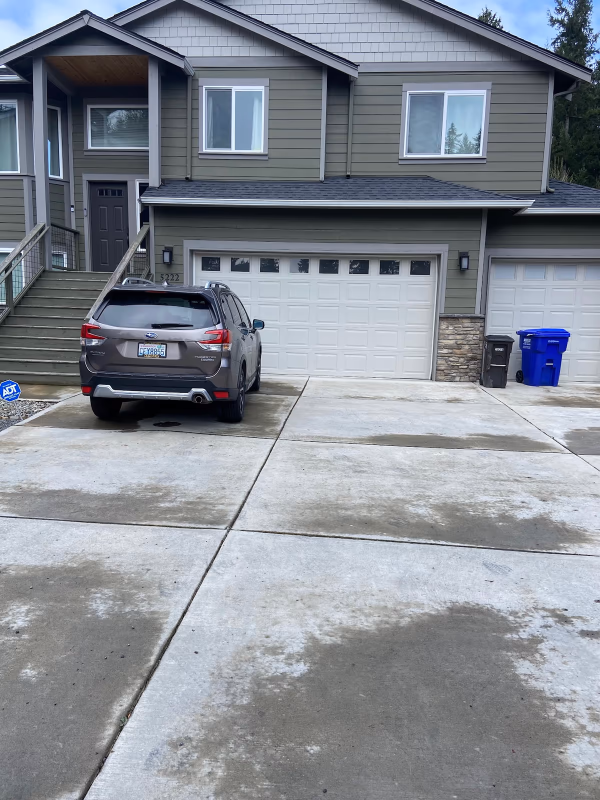 Residential two-story building with a front garage, driveway, stairs, and a parked SUV.