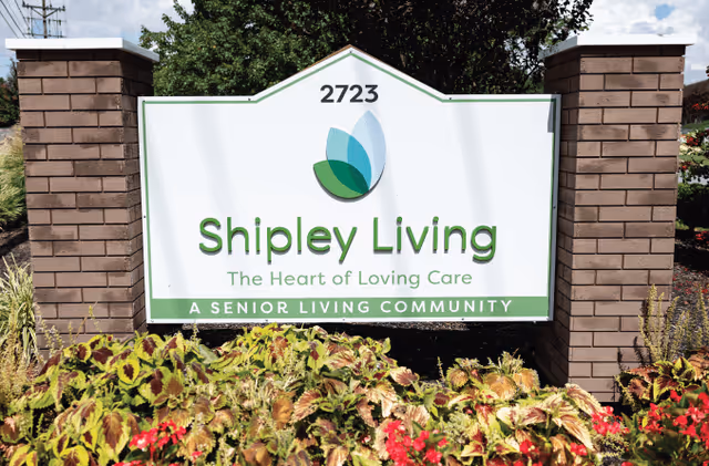 Exterior sign for Shipley Living at a senior community, framed by brick pillars and plants.