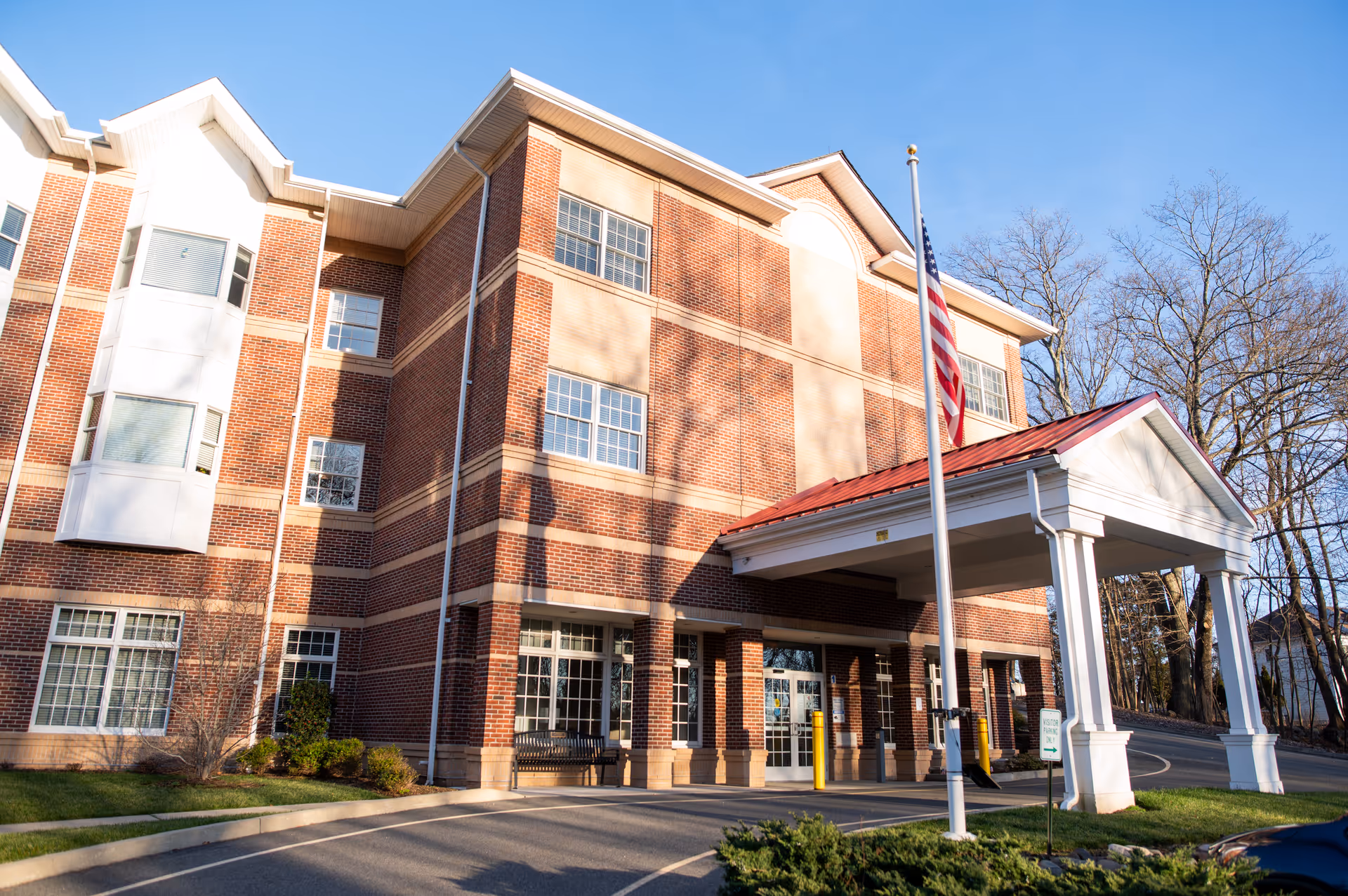 Exterior view of Windmere, a brick senior living facility, with porte-cochère and flag.