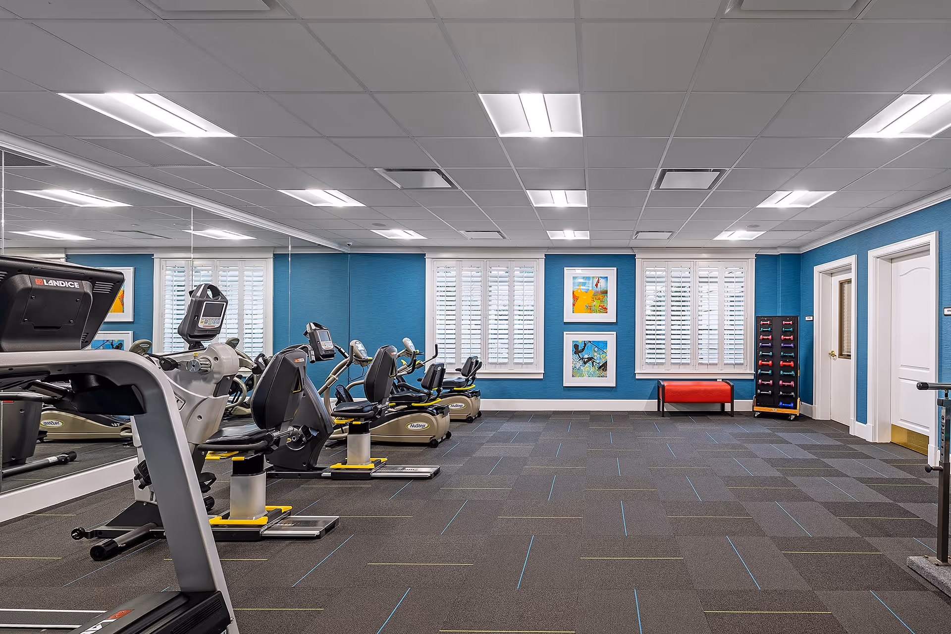 Bright exercise room with treadmills, bikes, and blue-walled gym area in a senior facility.