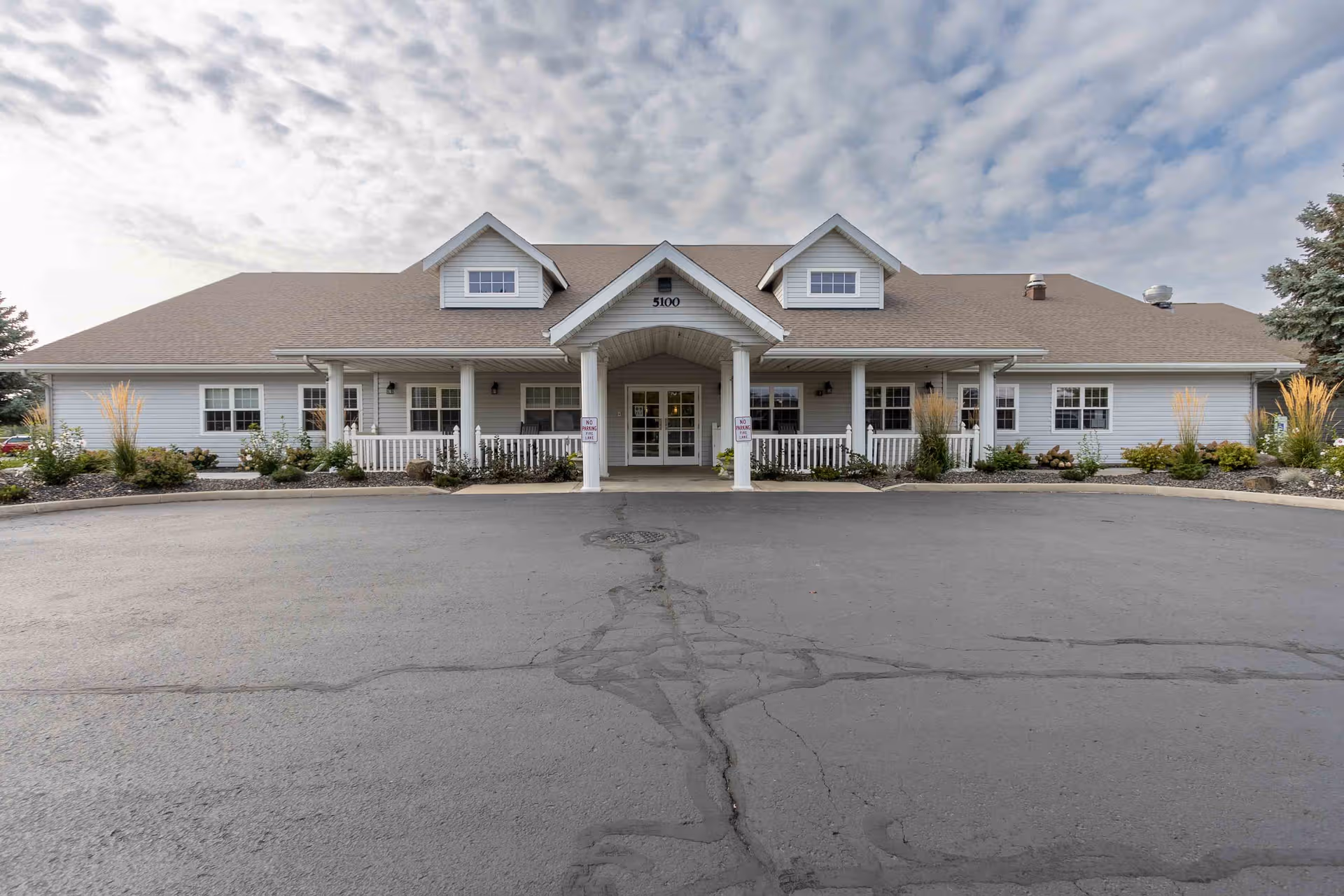 Front view of a single story senior living building with a central entrance and parking lot.