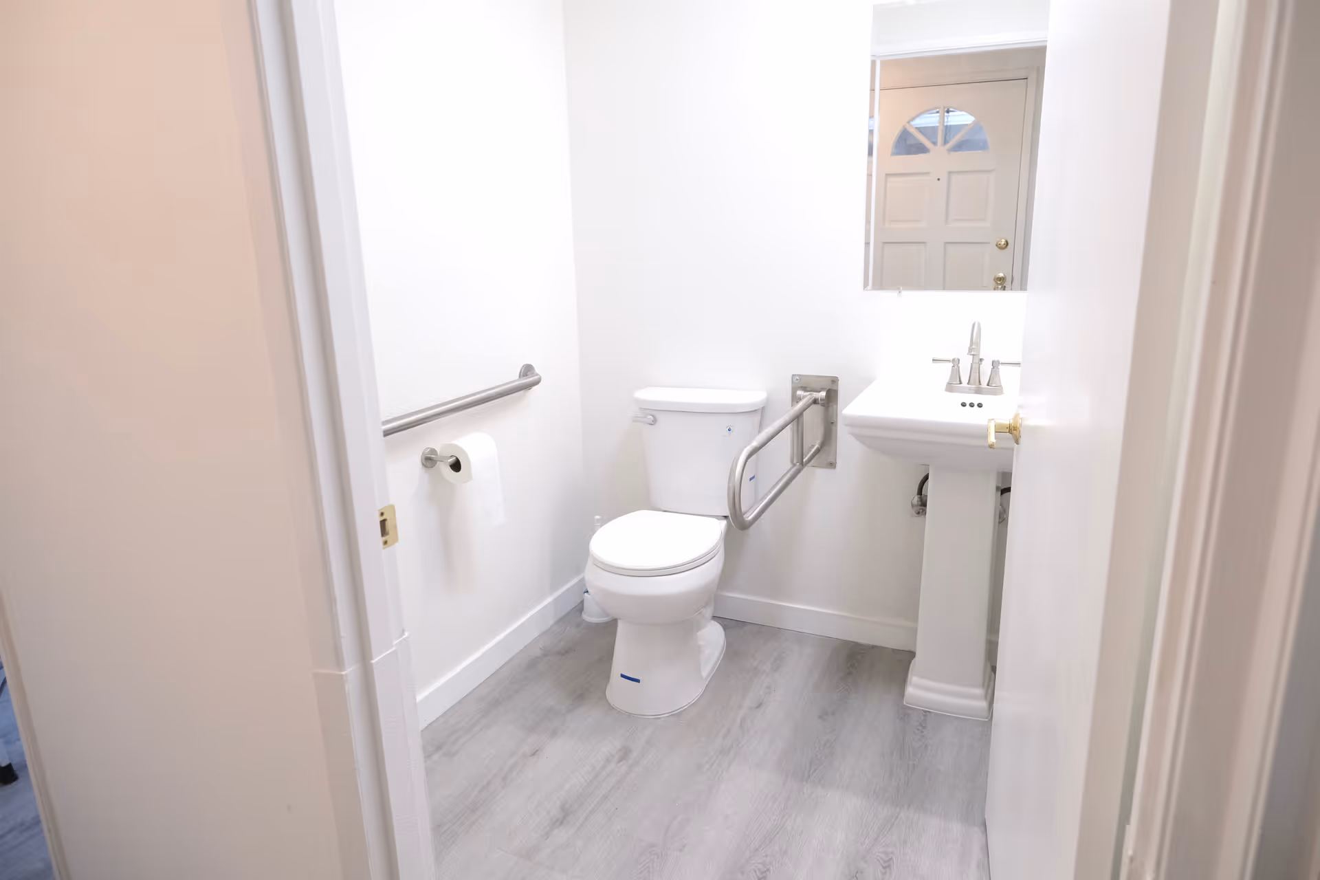 Accessible bathroom with grab bars, toilet, sink, and mirror.
