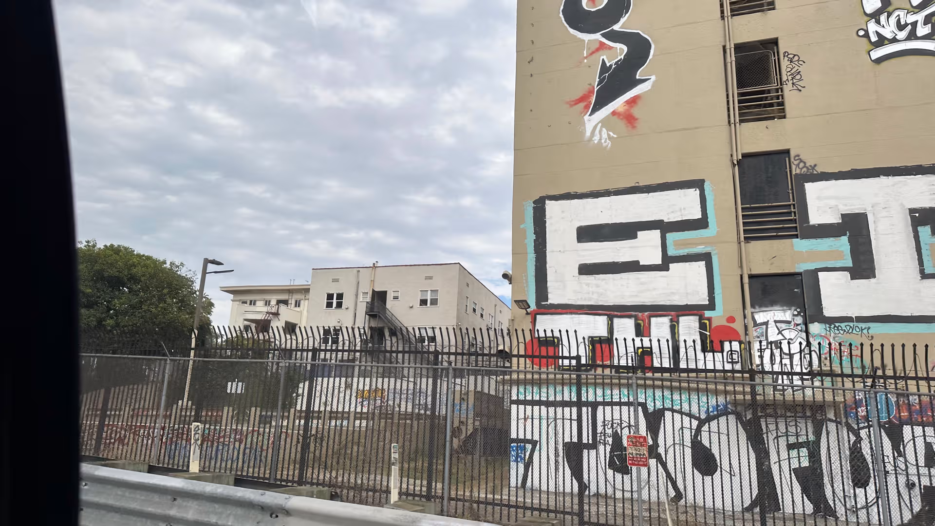 Graffiti-covered building exterior with a tall fence and smaller building behind.