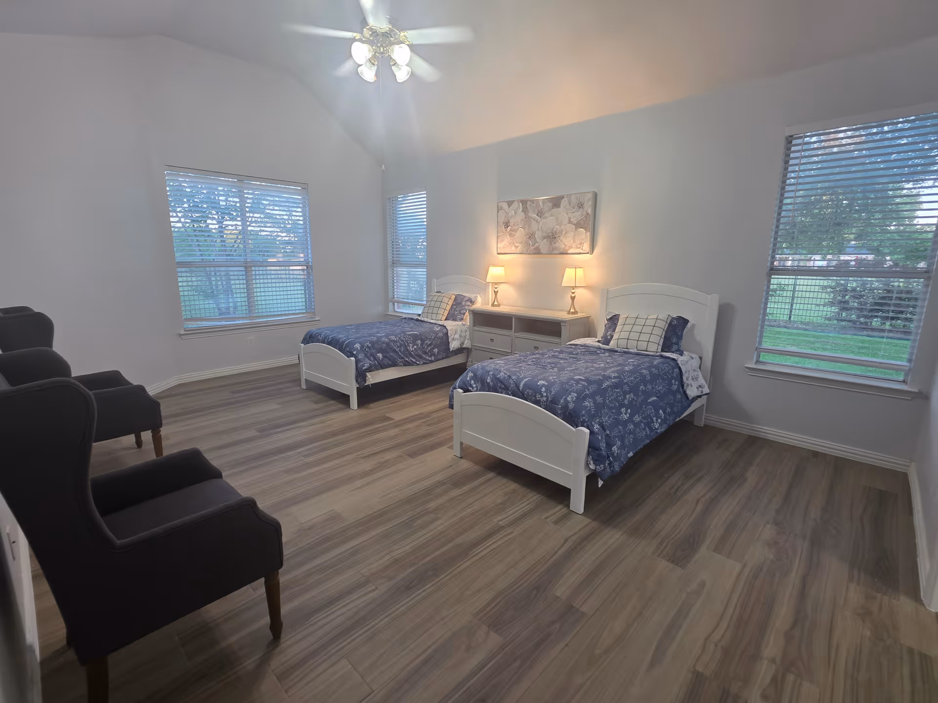 Two white bed frames with blue bedding and a dresser flank twin beds in a bedroom.