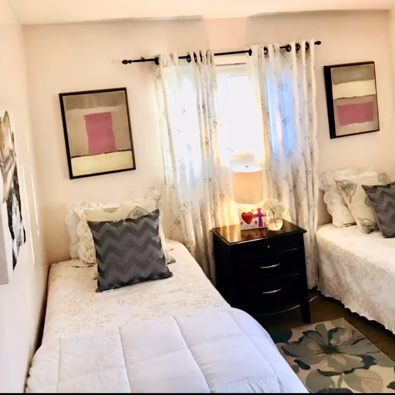 Two single beds with a nightstand between, in a bright, cozy bedroom.