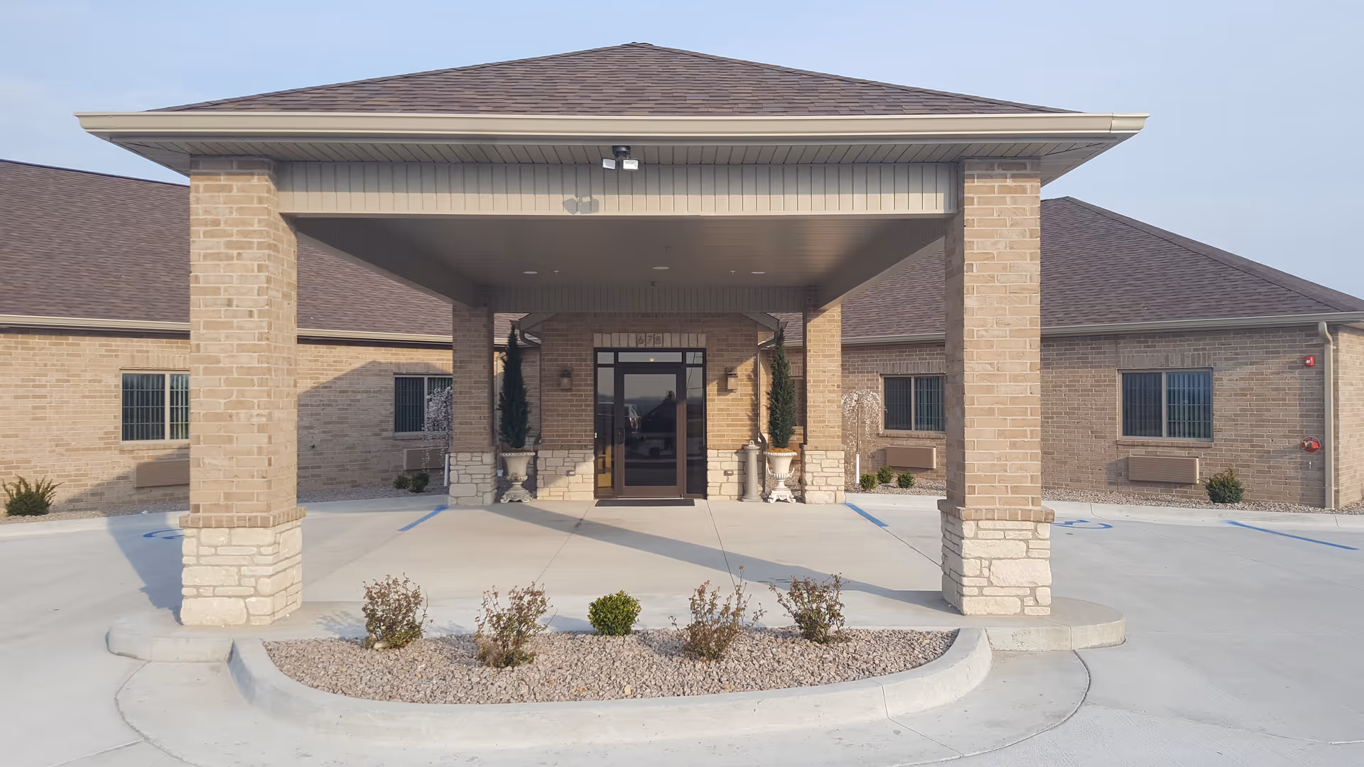 Front entrance of a brick retirement center with a covered drive and landscaping.