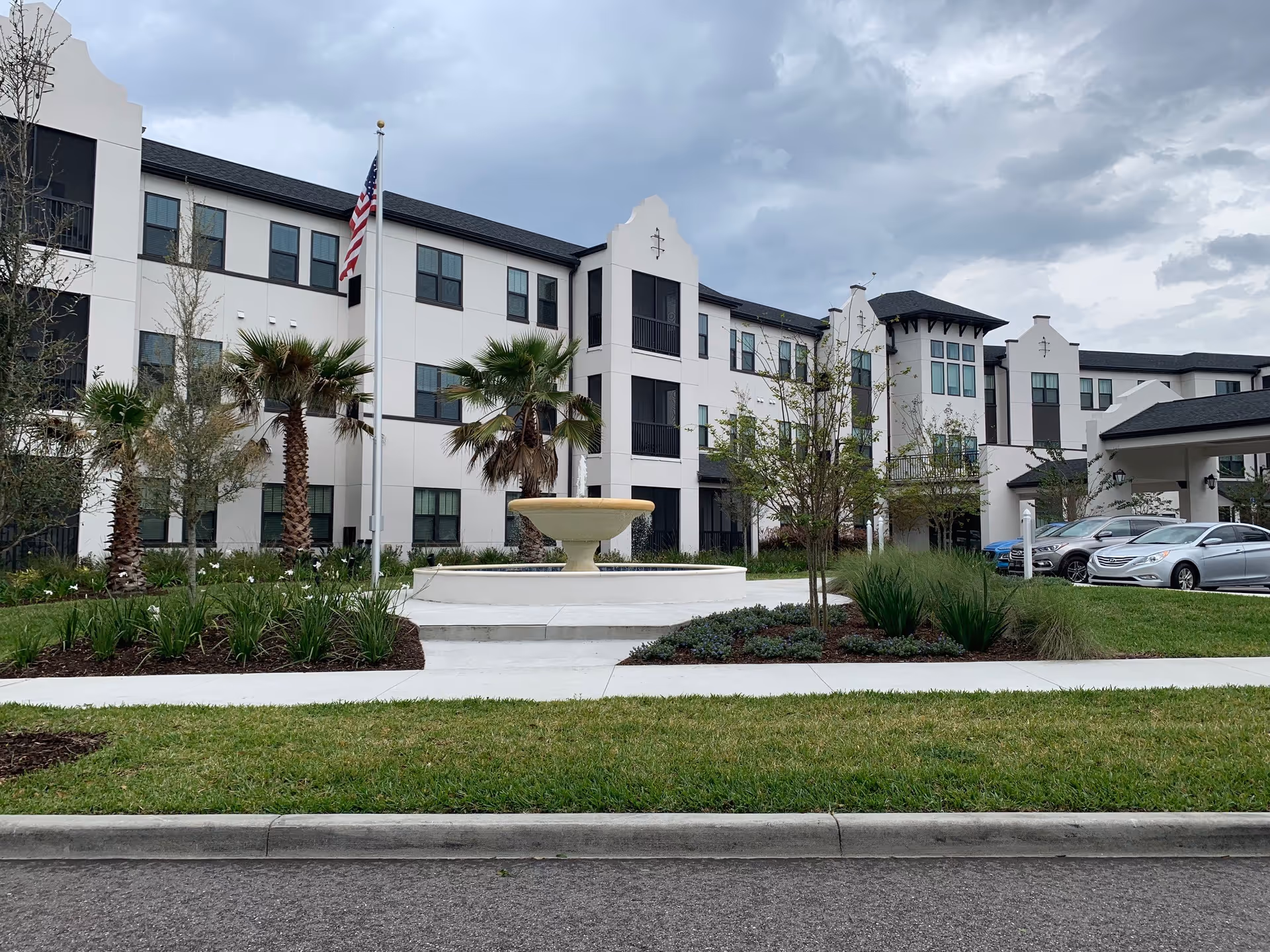 Exterior view of The Grove at Trelago with fountain, palm trees, and parked cars.
