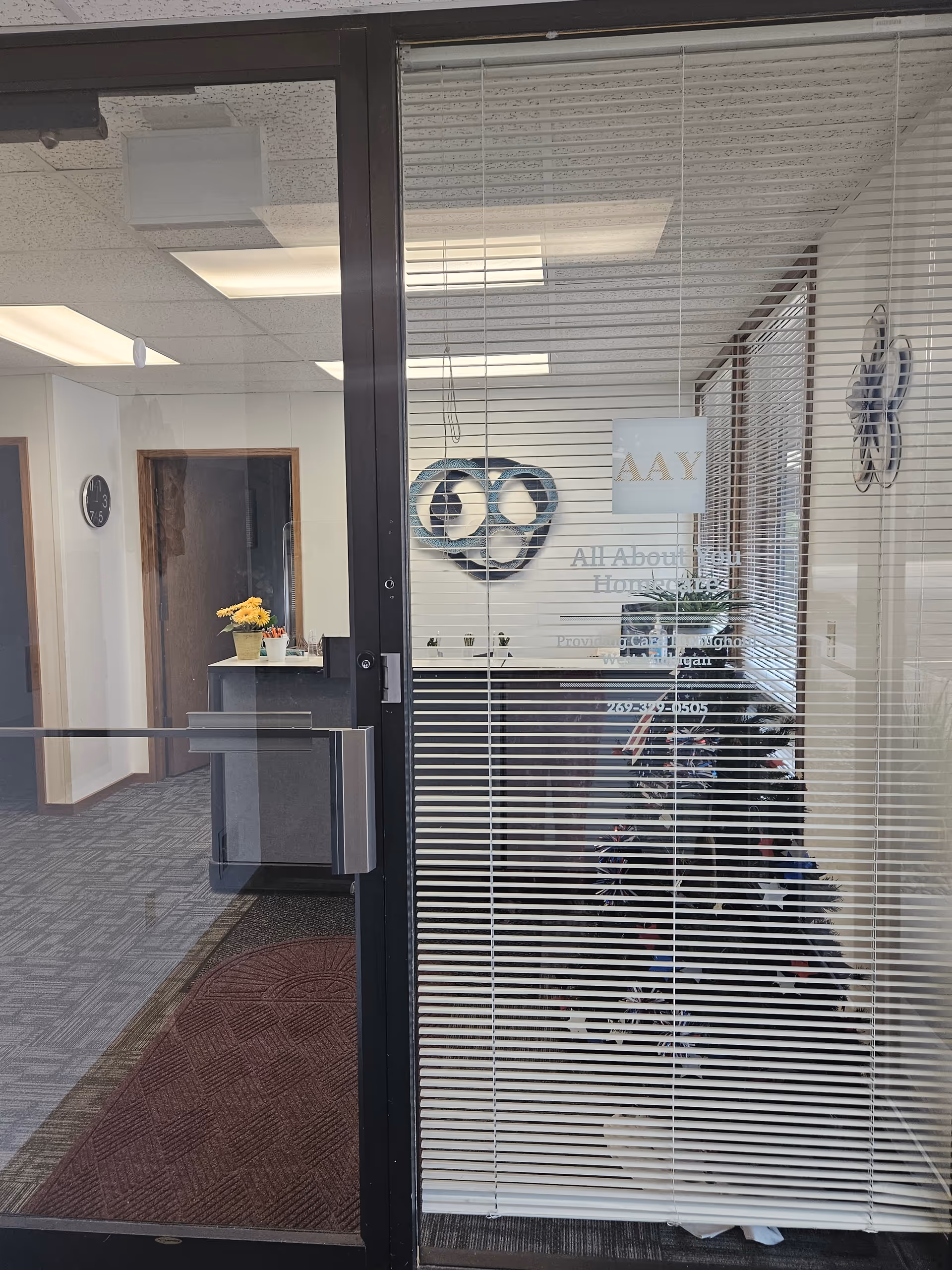 Glass entrance to All About You Homecare lobby with blinds and a reception desk.