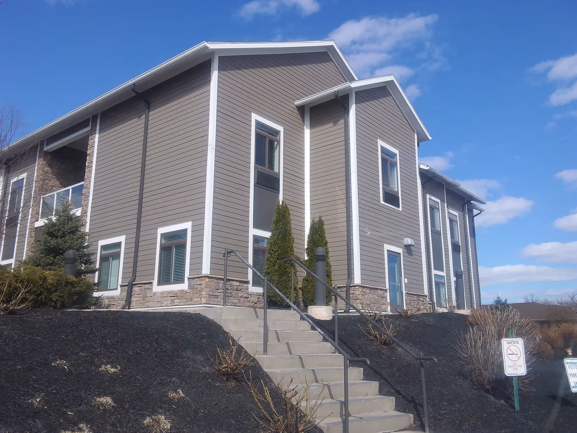 Exterior view of a modern senior living facility with stairs, landscaping, and stone accents.