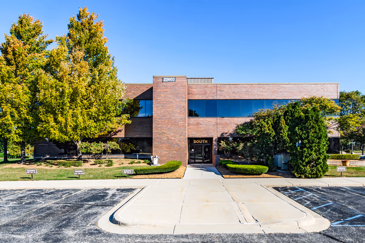 Brick senior living facility exterior with a central entrance and landscaped shrubs.