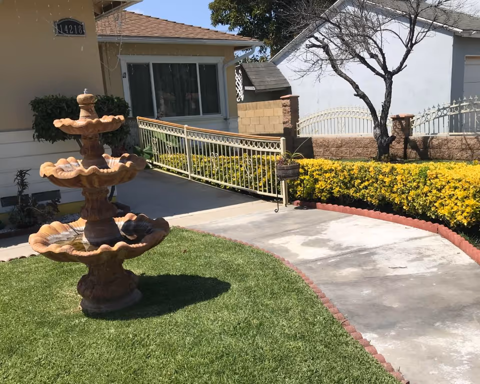Front yard of Baldwin Gracious Living with a tiered fountain, walkway, and hedges.
